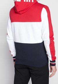 Bluza z kapturem w kolorach czerwonym, białym i granatowym, z blokami kolorów. Miękka tkanina z prążkowanymi mankietami. Duże logo nadrukowane na czerwonym kapturze.