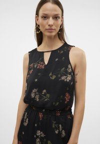 Top senza maniche nero con scollatura a chiave, caratterizzato da un motivo floreale in colori tenui. Tessuto leggero con una vestibilità rilassata e una consistenza morbida.