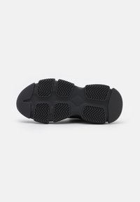 Semelle de chaussure de sport noire en caoutchouc texturé, avec un motif en zigzag pour l'adhérence et des bords arrondis lisses.