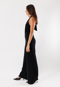 Jumpsuit nero con scollo all'americana, vita elasticizzata e design a gamba larga. Realizzato in tessuto liscio, con dettaglio di legatura sul retro.