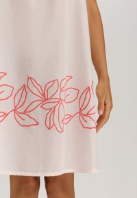 Vestido rosa con un patrón floral en bordado color coral a lo largo del dobladillo. La tela es ligera y de textura suave.