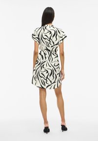Weißes Kleid mit einem schwarzen abstrakten Zebra-Muster, mit kurzen Ärmeln, einer taillierten Taille und einem knielangen Saum.