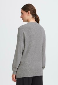 Grau gestrickter Pullover mit einem einfachen Rundhalsausschnitt und Rippbündchen, der einen lockeren Schnitt und einen längeren Rückenbund für zusätzlichen Schutz bietet.