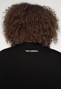 T-shirt nera con scollatura rotonda. Il retro mostra la scritta "KARL LAGERFELD" in bianco. La texture appare morbida e liscia.