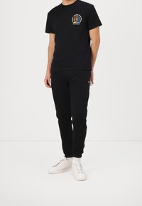 Svart bomulls t-shirt med en mångfärgad lejongrafik och text på bröstet, kombinerad med svarta sweatpants och vita sneakers.