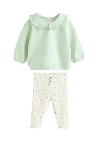 Sweat-shirt vert clair avec un col volants et des poignets élastiques, accompagné d'un pantalon blanc à côtes avec un motif floral et des accents de boutons.