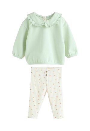 Hellgrüner Sweatshirt mit einem gerafften Kragen und elastischen Bündchen, kombiniert mit weißen gerippten Hosen mit floralem Muster und Knopfdetails.