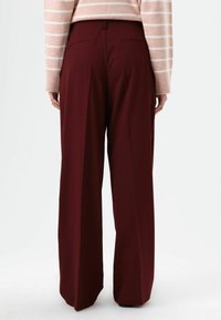 Bordeauxrote weit geschnittene Hosen mit hoher Taille, Falten und Gesäßtaschen, gefertigt aus einem glatten Stoff mit maßgeschneiderter Passform.