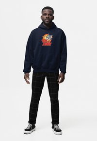 Felpa blu marina con grafica di "Tom e Jerry", caratterizzata da personaggi dei cartoni animati. Abbinata a pantaloni neri a quadri e sneakers nere.