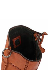 Sac en cuir marron avec des accents cousus, fermeture éclair et anneau en métal. L'intérieur présente une doublure sombre et une petite poche zippée.