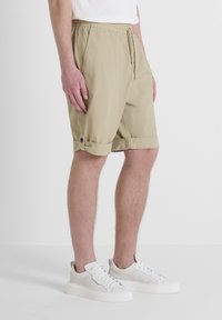 Pantaloni corti beige con cintura elastica e cordoncino. Risvolti fissati con un bottone. Indossati con sneakers bianche. Tessuto piatto.