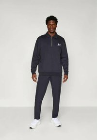 Námořnická mikina na zip s límcem a logem, doplněná o odpovídající zúžené kalhoty a bílé tenisky; hladká textura, sportovní design.