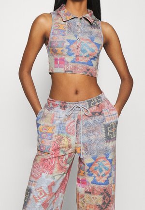 Bezrękawny krótki top polo i pasujące spodnie ze sznurkiem, z wielokolorowymi, abstrakcyjnymi wzorami geometrycznymi i kwiatowymi, noszone przez osobę.