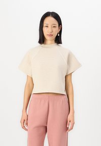 Cropped sweatshirt beige corto con maniche corte, caratterizzato da un collo alto e cuciture raglan, abbinato a pantaloni della tuta rosa.
