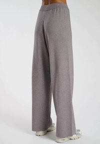 Grå vida byxor i mjukt tyg med en platt midja. Byxorna har en avslappnad passform och sträcker sig ner till anklarna.