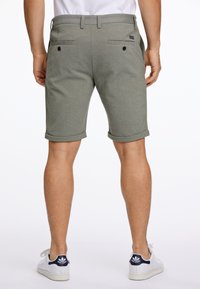 Grau-gestrickte Baumwollmix-Shorts mit umgeschlagenen Säumen, zwei Gesäßtaschen und schwarzen Knöpfen. Kombiniert mit weißen Sneakers mit marineblauen Akzenten.