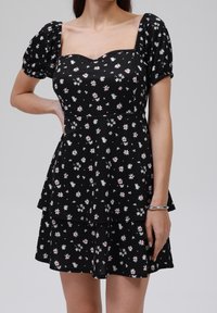 Černé šaty s krátkými nafouknutými rukávy, čtvercovým výstřihem a vrstveným peplum designem. Mají květinový vzor v bílé a růžové barvě. Měkka textilie.