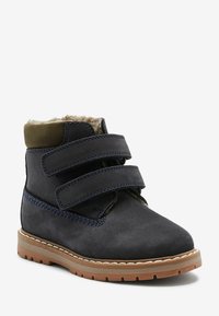 Dunkelblaue Wildlederstiefel mit einem wärmenden Innenfutter, zwei verstellbaren Klettverschlüssen und einer Gummisohle. Akzentuiert mit olivgrünen Details an der Oberkante.
