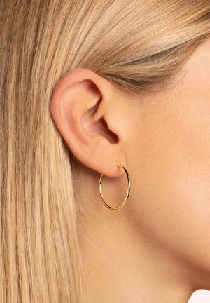 Goldene Creolen, dünnes und kreisförmiges Design, glatte Oberfläche, hängen vom Ohrläppchen neben hellblondem Haar.