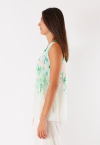 Blusa senza maniche in tessuto bianco trasparente; presenta una stampa floreale verde con morbidi accenti pesco; vestibilità rilassata, orlo arrotondato e leggera trasparenza.