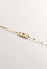 Pulsera de tono dorado con un diseño de cadena, que presenta un gran encanto en forma de clip de papel como detalle central. La cadena está intrincadamente enlazada y es suave.