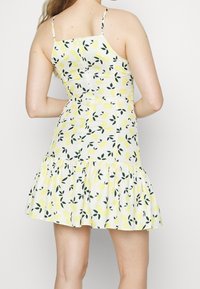 Robe blanche avec imprimé citron et feuilles. Présente des fines bretelles, un corsage ajusté et un ourlet évasé avec volants. Texture semblable au coton.