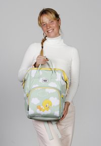 Mochila verde con patrón de nubes, acentos amarillos y gráfico de Tweety Bird. Cuenta con dos asas y compartimentos con cremallera.