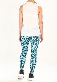 Biała bezrękawnikowa bluzka z okrągłym dekoltem, zestawiona z niebieskimi legginsami w abstrakcyjne wzory imitujące pociągnięcia pędzla, noszona z czarnymi butami sportowymi.