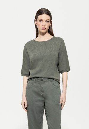 Olivenfarbener Strickpullover mit kurzen Ärmeln, Rundhalsausschnitt und strukturierter Oberfläche, kombiniert mit passenden olivenfarbigen Hosen mit seitlichen Taschen.