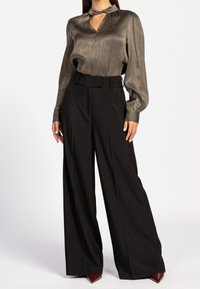 Blouse en bronze métallisé à manches longues avec un col en forme de goutte, associée à un pantalon noir taille haute à jambes larges. Textures lisses et coupe structurée.