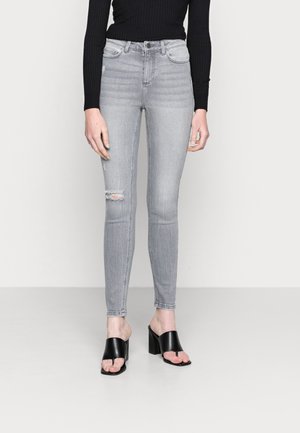 Jeans skinny cinza com detalhes desgastados, design de cintura alta e textura suave, combinados com sandálias pretas de salto bloco.