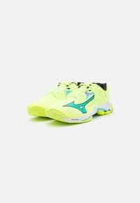 Zapatillas deportivas de color amarillo neón con acentos negros y detalles en turquesa. Cuentan con suelas texturizadas y un diseño elegante adecuado para el deporte.