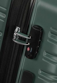 Valigia rigida verde con finitura testurizzata, dotata di lucchetto TSA nero, doppie cerniere e dettagli in metallo.