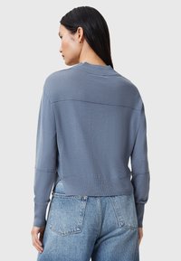 Lichtblauwe gebreide trui met lange mouwen, geribbelderand en detail in de naad op de rug, gecombineerd met high-waisted, vervaagde blauwe spijkerbroek.