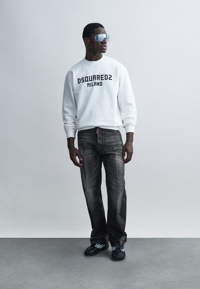 White sweatshirt with black "DSQUARED2 MILANO" text, paired with dark gray distressed jeans and black athletic shoes featuring white accents.