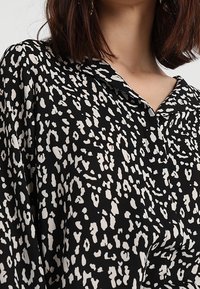 Černá blůza s leopardím potiskem v bílé barvě, s límečkem a zapínáním na knoflíky. Vyrobeno z lehkého materiálu.