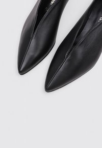 Chaussures en cuir noir à bout pointu avec un design épuré et une texture lisse. Présentent une découpe sur le côté pour un look moderne.
