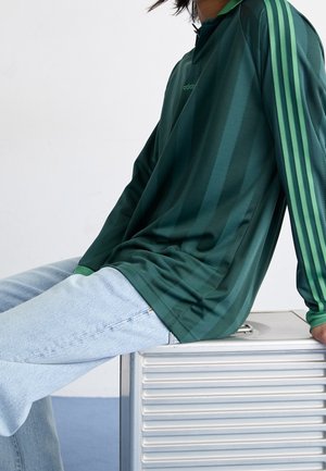 Grünes Langarm-Polohemd mit vertikalen Streifen, aus glattem Material. Verfügt über das Adidas-Branding und kontrastierende grüne Akzente an den Ärmeln.