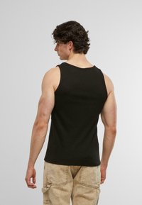 Schwarzes Tanktop mit figurnaher Passform, Rundhalsausschnitt und gerippter Textur, kombiniert mit hellen Cargo-Hosen. Ansicht von hinten.