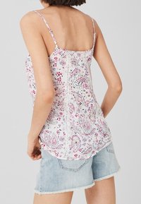 Camiseta sin mangas con estampado floral en tejido ligero, tirantes ajustables tipo espagueti, base blanca y detalles en rosa y púrpura, combinada con pantalones cortos de denim claro.