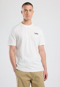 Camiseta de algodón blanca con cuello redondo y mangas cortas, que presenta texto bordado en negro "Brooklyn Coffee Shop" en el área izquierda del pecho.