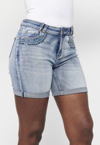 Shorts en denim bleu clair avec ourlets roulés. Présente une décoration en perles bleues sur les poches avant, avec un design classique à cinq poches.
