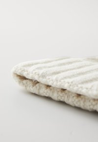 Tessuto lavorato a maglia morbido di colore crema, caratterizzato da una texture a costine e un design piegato. Il bordo ha una finitura morbida e fluffosa.