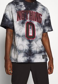 Camiseta de manga corta en tie-dye en blanco y negro, con la impresión en rojo de "NOTHING" y un "0" prominente en el frente, con tejido texturizado.