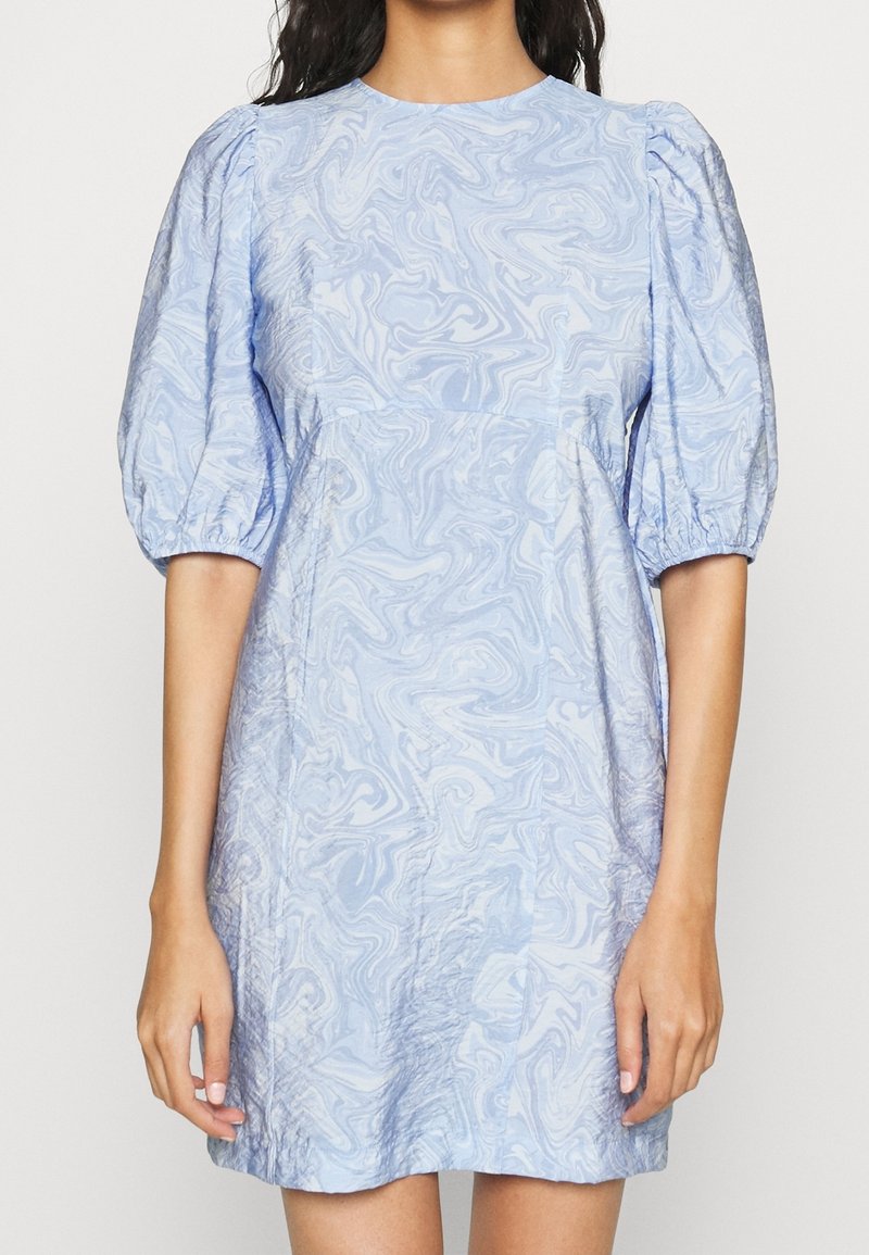 Ljusblå klänning med puffärmar, tillverkad av texturerad tyg med ett marmormönster. A-linjeprofil med rund halsringning och sömdetaljer.