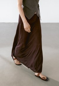 Lange, vloeiende paarse rok gecombineerd met een grijze aansluitende top, aangevuld met bruin en zwarte sandalen, met een gladde textuur en eenvoudig ontwerp.