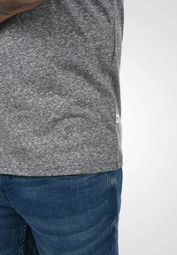 Grå T-skjorte med korte ermer laget av teksturert stoff, med en sideventilasjon og et lite merke, kombinert med blå denimjeans.