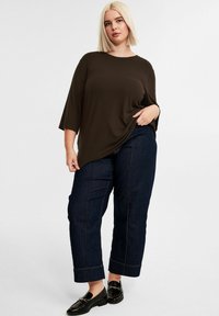 Ruskea ribattu toppi löysällä istuvuudella, yhdistettynä tummiin denim-housuihin, joissa on käänteet ja erottuva ompelu. Mustat loafersit viimeistelevät asun.