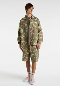Camouflage jacket and shorts in green, brown, and beige. Lightweight fabric with elastic cuffs, layered look, and logo detail.
