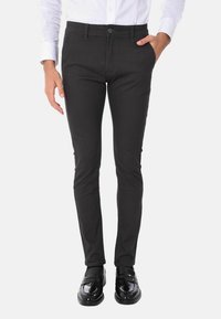 Pantaloni neri slim-fit realizzati in tessuto testurizzato, con chiusura a bottoni e tasche laterali, indossati con Mocassini neri lucidi e una camicia bianca.
